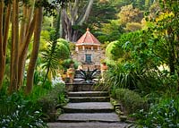View into the Mediterranean garden with steps, Agave Fountain by Tom Leaper, wall fountain and Shell House, Tresco Abbey Garden, Tresco, Isles of Scilly. 