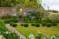 The front garden with lawn, box balls and stone wall with archway. 
