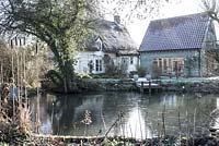 Thatched cottage with pond and wooden jetty on a frosty morning. St Francis Cottage