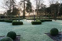 Early morning sun filters through trees to illuminate the formal garden to the south of the house. Welford Park, Newbury, Berks, UK