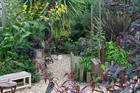 Driftwood, gravel and rusted iron are signature materials in this garden of curving spaces, softened by the textural foliage planting, including Inula magnifica, Cotinus coggrygia, Cordyline, Phormium and Pinus mugo. In the foreground: Physocarpus opulifolius 'Diabolo' and Persicaria microcephala 'Red Dragon'.