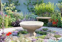 Water feature by Andrew Ewing surrounded by circle of herbs including various varieties of Thymus such as 'Iden', 'Jekka' and 'Porlock' - A Modern Apothecary, The St John's Hospice Garden. RHS Chelsea Flower Show 2016. Designer: Jekka McVicar, Sponsor: St John's Hospice