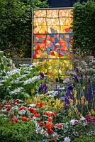 Evening in God's Own Country - A Garden for Yorkshire, with Geum, Salvias, Irises, Roses, Stipa gigantea, Viburnu 'Mariesii', lit by a modern stained window, inspired by York Minster. The RHS Chelsea Flower Show 2016. Designer: Matthew Wilson- Sponsor: Welcome ot Yorkshire - SILVER -PEOPLES CHOICE BEST SHOW GARDEN