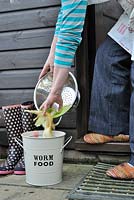 Composting kitchen waste, woman placing, kitchen waste into recycling bin outside kitchen door, Norfolk, UK, October