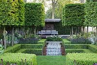 The Husqvarna Garden, view of bluestone cobbles steps and path in centre of formal garden leading to modern patio and surrounded by medium high Buxus hedges, a flowerbed with purple flowers, Lysimachia atropurpurea 'Beaujolais' and  Carpinus pleached - floating cubes. RHS Chelsea Flower Show, 2016