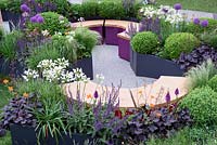 The Urban Connection Garden. Oak Top semi circular seats surrounded by extensive planting in containers. The RHS Chelsea Flower Show 2016, Designer: Lee Bestall Sponsors: Victoria Business Improvement District
