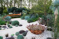 The Winton Beauty of Mathematics Garden, view of copper water feature, curved bench and desert-like sand path surrounded by Yucca rostrata, Dasylirion wheeleri, Pines, Echeveria 'Duchess of Nuremberg', succulents, tropical, Mediterranean plants. The RHS Chelsea Flower Show 2016, Designer: Nick Bailey, Sponsor: Winton