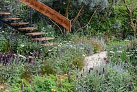 Stairs with copper banister surrounded by planting including Pinus sylvestris 'Glauca', Allium atropurpureum, Calendula officinalis 'Sherbet Fizz' in The Winton Beauty of Mathematics Garden. The RHS Chelsea Flower Show 2016 - Designer: Nick Bailey - Sponsor: Winton- SILVER GILT