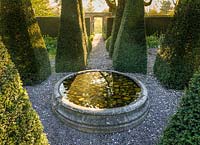 Dawn light shines through a gateway into The Well Garden with its pyramidal yews and tulips, at Wollerton Old Hall Garden, Shropshire - photographed in April