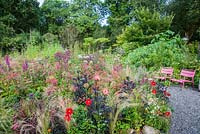 Bed near the house full of pink, red, purple and magenta herbaceous perennials and annuals including Dahlia 'Twyning's Revel', D. 'Poppyscotland', salvias, Filipendula purpurea 'Elegans', monardas, sedums and Astilbe chinensis var. taquetii 'Purpurlanze'. Hunting Brook Garden, Co Wicklow, Ireland