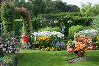 Colourful decorative bicycle holding pots with Begonia on a lawn and colourful mixed beds filled with bedding plants, perennials, Rosa, Buddleia and Clematis. 