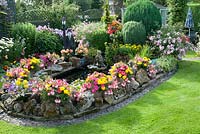 Colourful back garden with pond and rockery mixed borders filled with tender bedding plants, shrubs and perennials. 