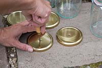 Using a bradle to create holes in the centre of the glass jar lids
