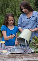 Two girls painting a galvanised bucket with a cream green paint