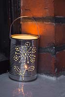 A lit tin can lantern sat on a window ledge