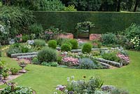A circular parterre with pink and blue planting including Sedum 'Matrona', Caryopteris 'Heavenly Blue', Agapanthus 'Blue Moon', Cleome hassleriana 'Rose Deep', Knautia macedonica, Cuphea viscosissima and Gladiolus murielae. Behind, a yew hedge with entrance surrounded by climbing roses.