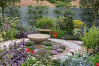 A Modern Apothecary. A courtyard for quiet reflection, planted with medicinal herbs. A circular brick and cobble path encloses a bed of thyme, at its centre a stone water basin created by Karl Friedrich. Designer: Jekka McVicar. RHS Chelsea Flower Show 2016