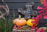 Oak tree slice painted and decorated to display 'We're in the garden' with Autumnal display
