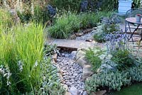 The Drought Garden. Stone bridge over dry stone river in gravelled city garden with drought tolerant planting. Designer: Steve Dimmock. RHS Hampton Court Palace Flower Show 2016