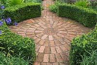 Circular brick paving surrounded by curved Buxus sempervirens hedges
