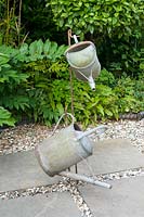 Suspended metal watering cans as a decoration on a patio and mixed border behind