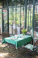 Outside the Art Deco glasshouse, wood and iron garden suite with green tablecloth
