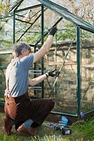 Man inserting glass pane into place - wearing protective gloves. The top pane of glass sits on small metal' z' clips: April, Spring.