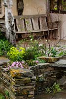 Rustic stone wall with naturalistic planting and weathered oak bench beyond - Macmillan Legacy Garden - RHS Malvern Spring Show 2016. Designer: Mark Eveleigh, Sponsor: Macmillan Cancer Support