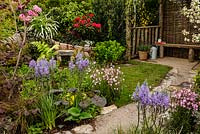 Rustic stone and gravel path leading to seating area through mixed colourful planting including Camassia - Camas lily - The Water Spout garden - RHS Malvern Spring Show 2016. Designer: Christian Dowle. Sponsor: Garden Inspiration