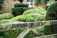 Cottage name in relief on the 5 bar gate, with mounds of clipped box and yew topiary in the front garden beyond.