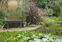 Seating area beside the pond with ornamental grasses, Phormium and a potted Equisetum japonicum