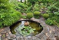 Circular pond with water lily and decorative urn.  Clipped box balls, relaxing area and borders. Frank Thuyls garden