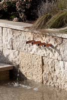 Four copper pipe spigots coming out of a wall with water spilling into a pond