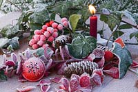 Lit red candle with frosted red bell bauble, Pine cones, Ivy foliage and Skimmia berries