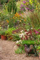 Gravel path, metal chicken ornament, sedum pennisetum, Helenium Sarins - informal country garden.  Owner of Daisy Roots Nursery, Anne Godfrey's own private garden, Hertfordshire, late summer