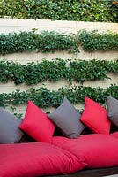 Inner city courtyard with bench seating with grey and red cushions and a brick wall with Trachelospermum jasminoides behind