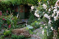View of summerhouse covered in Lonicera and Jasminus officinale. Other planting includes Roses, Centranthus ruber, Carex buchananii, Senecio, Aquilegia and Campanula persicifolia