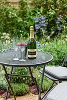 A round metal bistro table and chairs with champagne and aeonium in a metal flowerpot in the Drought Garden, RHS Hampton Court Flower Show 2016