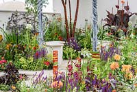 A metal pergola by Dragonswood Forge, Prunus serrula var. tibetica in corner surrounded by colourful planting including Salvia, Penstemon, Helenium 'Moerheim Beauty' and Canna 'Durban'. RHS Hampton Court Flower Show, 2016