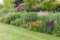 A long herbaceous border featuring plants such as Hemerocallis 'Corky', Foeniculum vulgare 'Purpureum', Salvia nemorosa and Geums at Bluebell Cottage Gardens