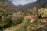 Aerial view of gardens with borders, terracotta roofed houses and tree covered hills beyond - Lake Atitlan Hotel, Guatemala