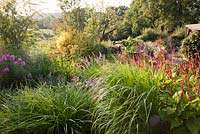 View from top terrace with Kniphofia Percys Pride, Persicaria amplexicaulis Firetail, Geranium Eureka Blue,  Phlox and Crocosmia  to countryside beyond