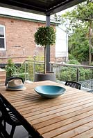Dining area with a timber topped table, a blue bowl, a mans straw hat, and a potted standard plant on an upper patio.
