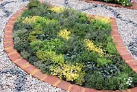 Mixed herb bed lined with bricks and surrounded by pebbles - Spa Garden - I follow the Waters and the Wind, RHS Malvern Spring Festival 2017 - Design: Annette Baines-Stiller