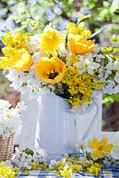 Display of spring flowers in jug. daffodils, tulips, mahonia and cherry blossom branches.