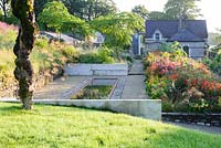 A grassy walk surrounds the densely planted, ornamental centre of the garden, giving fine views along the hot border back towards the former steward's house framed by the inverted dead tree trunk standing sentinel over the reflecting pool. Plants include Crocosmia 'Lucifer', day lilies, Cotinus 'Grace', dahlias and ligularias. 