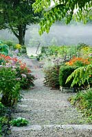 A stone edged path leads towards the mist shrouded field below the garden past planting including Eupatorium cannabinum, fuchsias, Crocosmia 'Lucifer', heleniums, angelica and grasses.