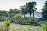 Misty late summer morning at June Blake's garden, viewed from the hillside above colourful beds full