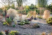 Gravel garden in front of the house includes many grasses and herbaceous perennials plus black Ophiopogon planiscapus 'Nigrescens' and a metal sheep sculpture with moss covered troughs in the foreground. Windy Ridge, Little Wenlock, Shropshire, UK