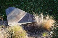 Simple slate seat in the gravel garden surrounded by deciduous grasses. Windy Ridge, Little Wenlock, Shropshire, UK